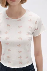 Remera blanca con estampado de moños rosas y lunares. Tiene cuello redondo y mangas cortas con terminación ondulada.