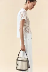 Bolso tipo bucket cilíndrico a rayas verticales en tonos beige y blanco, con asa de mano trenzada color marrón y asa de hombro extraíble. Incluye bolso de tela interior y pespuntes a contraste.