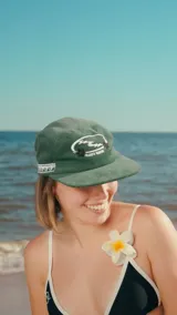 Gorra verde de pana con diseño de cinco paneles, visera curva y logo bordado en el frente.