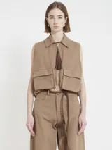 Chaleco marrón de gabardina con corte recto y estilo utilitario. Tiene cierre frontal con tirador de flecos largos en cuero y bolsillos grandes con tapa en el frente.
