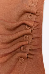Top color ladrillo de punto con cuello redondo amplio y hombros descubiertos. Detalle de frunces delanteros y botones laterales forrados a tono.