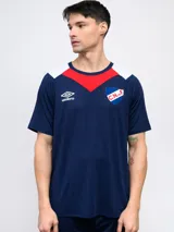 Remera de fútbol Umbro del Club Nacional de Football, modelo de entrenamiento. Diseño azul con detalles en blanco y rojo en cuello y mangas. Incluye logo de Umbro y escudo del club en el frente.