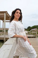 Túnica blanca con rayas verticales finas color dorado, corte holgado, mangas cortas amplias y lazo en la cintura.