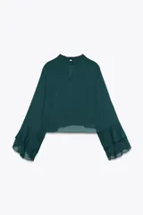 Camisa verde esmeralda de cuello alto y manga larga con volantes en los puños. Cierre en la espalda con abertura y botones.