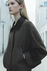 Chaqueta corta de tweed gris con cuello solapa y puños de cuero negro. Cierre frontal con botones ocultos.