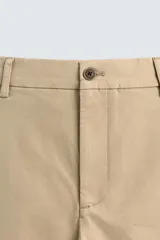 Pantalón chino color beige, de corte recto y tiro medio. Confeccionado en tejido de algodón con elasticidad, con bolsillos laterales y traseros de vivo. Cierre frontal con cremallera y botón.