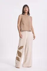 Pantalón ancho de lino color beige claro con estampado grande de hojas en color marrón en la parte inferior de la pierna izquierda. El pantalón tiene un corte holgado y tiro alto.