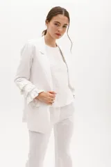 Blazer color beige confeccionado en lino, con cuello solapa, cierre frontal con un botón y mangas largas con volantes en capas.