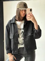 Campera negra de corte recto, con cuello camisero, cierre frontal con botones a presión, bolsillos de parche con solapa en el pecho y mangas largas con puños abotonados.