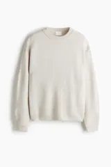 Buzo de tejido suave color beige, con cuello redondo acanalado, hombros caídos, mangas largas y puños y bajo en punto acanalado.