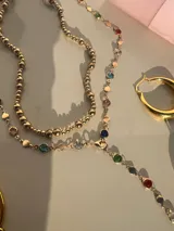 Set de dos collares dorados: uno tipo choker con esferas y otro tipo corbatín con dije de cadena con piedras de colores.