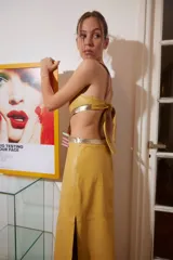 Vestido midi de cuero color maíz con cortes laterales y detalles dorados. Tiene tiras finas fucsias y abertura lateral en la falda.