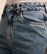 Bermuda de jeans azul con corte mom, tiro alto, cierre con botón y cremallera, y apliques de strass en el frente.