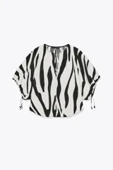 Top de cuello redondo y escote pico con estampado animal print cebra en blanco y negro. Manga corta abullonada ajustable con lazadas.