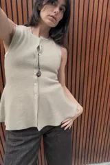 Top de punto acanalado en color beige, sin mangas y con cuello redondo. Presenta un cierre frontal con botones pequeños y un bajo con acabado en peplum que aporta volumen.