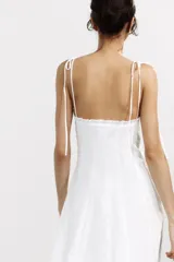 Vestido midi blanco de popelín con escote corazón y volantes. Tiene tirantes finos con detalle de lazo, forro interior combinado y cierre lateral con cremallera oculta.