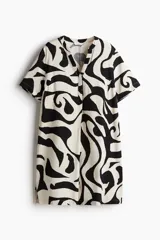Vestido túnica a la rodilla de viscosa con estampado abstracto en blanco y negro. Tiene cuello mao, abertura en V, corte holgado, hombros caídos, mangas cortas, bajo recto y tajos laterales.
