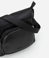 Bolso tipo postman negro, confeccionado en poliuretano, con bolsillo delantero y correa ajustable.
