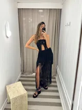 Falda larga de tejido de punto blanco, con cintura elástica y aberturas laterales. Presenta un largo fleco en el ruedo que cae hasta el suelo.