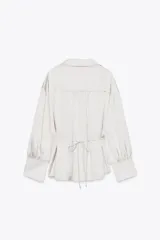 Camisa color blanco hueso de satén, con cuello solapa, escote en pico y mangas largas con puños abotonados.