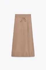 Falda midi color beige confeccionada en hilatura con viscosa. Tiene tiro alto, cintura con trabillas ajustable con lazada en el mismo tejido, detalle de doble pliegue en el delantero y bajo acabado con costuras marcadas a tono. Cierre lateral con cremallera oculta.