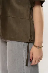 Remera color verde militar de gamuza, con cuello redondo, mangas cortas y detalle de cordones ajustables en el ruedo.