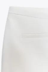 Falda pantalón corta color blanco, de tiro medio con bolsillos delanteros y cintura asimétrica. Cierre lateral con cremallera oculta.