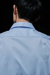 Camisa celeste de algodón con cuello italiano, tapeta clásica y canesú en la espalda. Mangas largas con tapeta y botón, y cierre ajustable de botón en los puños. Bajo levemente redondeado. Corte ajustado que realza el contorno del cuerpo creando una silueta entallada.