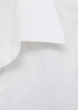 Camisa blanca de lino con cierre de botones en la parte delantera, mangas largas con puños abotonados, cuello camisero y corte recto. Incluye cinturón trenzado negro.