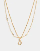 Collar corto doble dorado, con una cadena de eslabones y otra de eslabones retorcidos. La cadena más corta tiene circonitas engarzadas y la más larga tiene un dije circular con circonitas de colores.