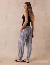 Pantalón largo de lino y rayón a rayas verticales grises y blancas. Tiene pretina elastizada con lazo de ajuste, bolsillos delanteros y traseros.