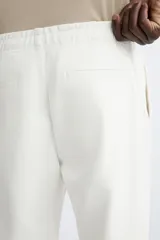 Pantalón de jogging color beige confeccionado en tejido de mezcla de algodón. Cuenta con cintura elástica ajustable con cordón, bolsillos frontales y traseros.