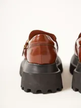 Mocasines marrones de cuero con hebilla dorada y plataforma track negra.