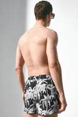 Short de baño negro con estampado de palmeras blancas, cintura elástica con cordón ajustable, bolsillos laterales y trasero.