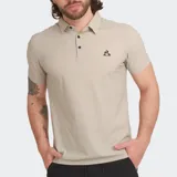 Polo de manga corta color beige, con cuello y tapeta de botones negros. Presenta el logo de Le Coq Sportif bordado en negro en el pecho.