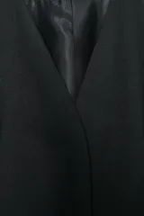 Blazer negra entallada, de escote pico y manga larga con hombreras. Tiene bolsillos delanteros de vivo y cierre frontal con botones a presión ocultos.