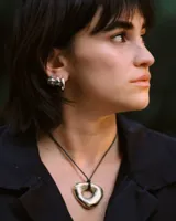 Collar con dije dorado irregular con agujero central, colgando de cordón negro ajustable.