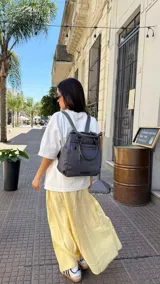 Mochila bandolera color marrón con herrajes color peltre. Tiene un compartimento principal amplio con cierre, un bolsillo frontal con cierre y dos bolsillos laterales abiertos. Incluye correa ajustable para usar al hombro o cruzada.