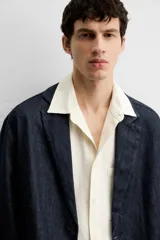 Blazer azul oscuro de denim, corte relaxed fit, con cuello de solapas de muesca, manga larga con puños abotonados, bolsillos de solapa en la cadera, abertura en el centro de la espalda y cierre frontal con botones. Sin forro interior.