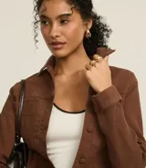 Campera marrón de sarga con textura cotelê, corte regular, cuello inglés, manga larga, abotonada y con bolsillos delanteros.