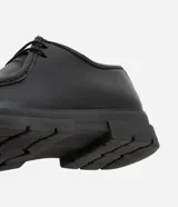 Zapato de vestir negro con cordones, fabricado en cuero sintético, con puntera redondeada y suela de goma.