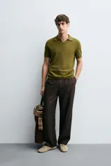 Jersey de punto color verde oliva, de calce relajado (relaxed fit), con cuello solapa y abertura frontal en forma de V. Es de manga corta y presenta acabados en rib en puños y ruedo.