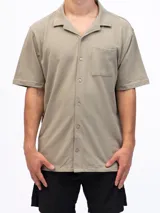 Camisa de manga corta color beige, confeccionada en tejido piqué de algodón, con cuello cubano y un bolsillo de parche en el pecho.