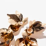 Aros colgantes dorados con forma de hojas y detalle de perla en la parte superior.