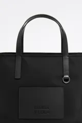 Bolso shopper mediano Bimba y Lola color negro, con doble asa de mano y correa bandolera ajustable y extraíble. Presenta un parche rectangular con el logo de la marca en la parte frontal.