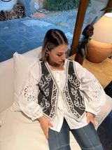 Chaleco negro con bordados florales blancos y ribete de crochet.