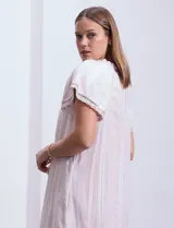 Vestido corto de lino a rayas verticales color lila y blanco, con cuello fruncido, escote en V y lazo de ajuste. Mangas cortas con puntilla de crochet.