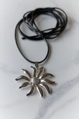 Collar con tiento negro y dije plateado en forma de flor con centro texturizado.