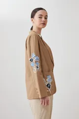 Blazer color tostado con bordados florales en azul y negro en la solapa y en la manga.