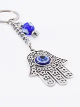 Llavero con dije de mano de Fátima (Hamsa) color plateado con ojo turco azul, y cuenta redonda azul con diseño de ojo turco.